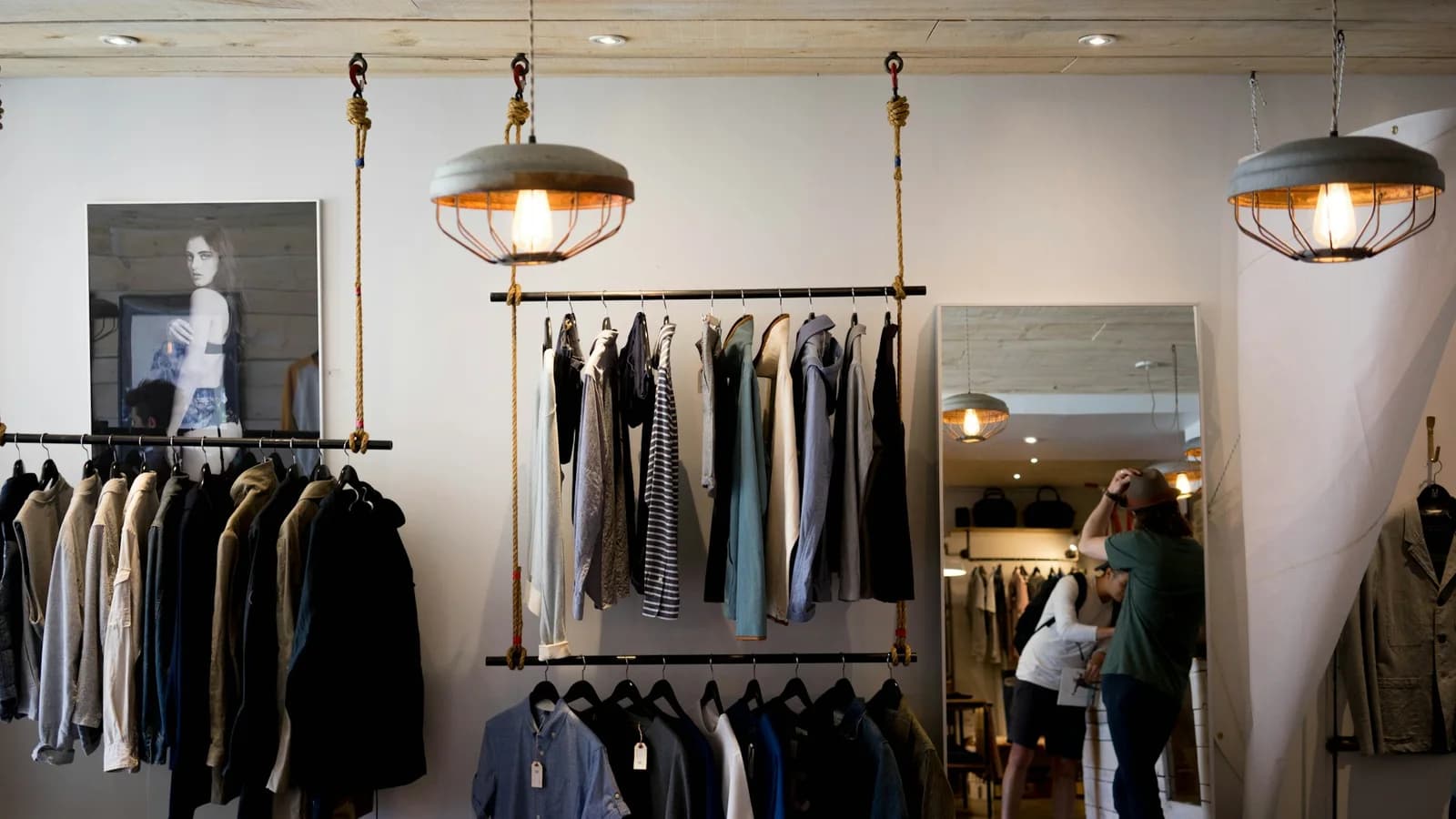 Interior de Clark Street Mercantile en Montréal, con prendas azules y grises, percheros suspendidos y lámparas sobre paredes claras.
